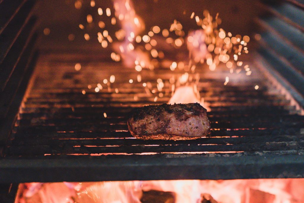steak cooking in oven grill surrounded by flames.