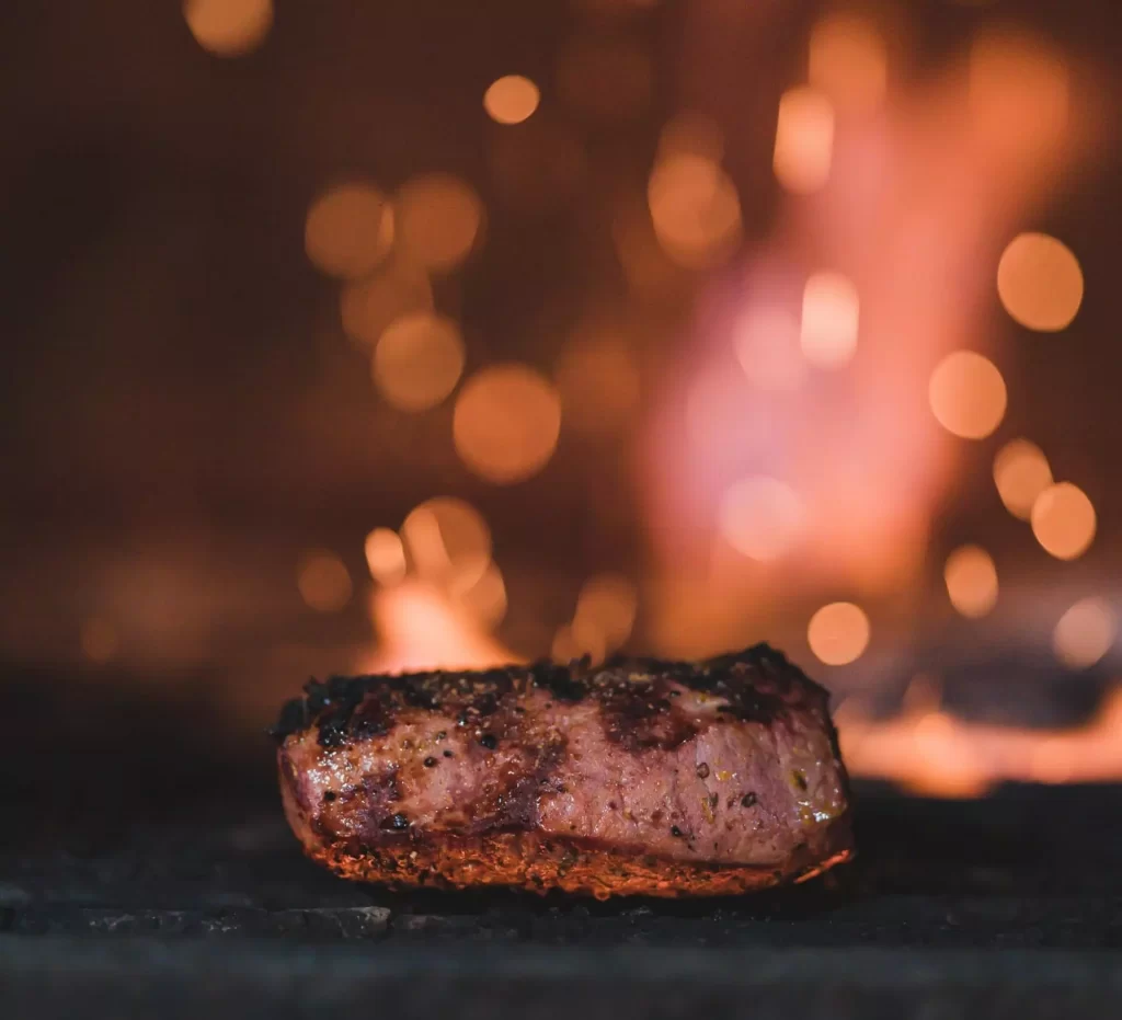 close up of steak with blurred flames in the background.