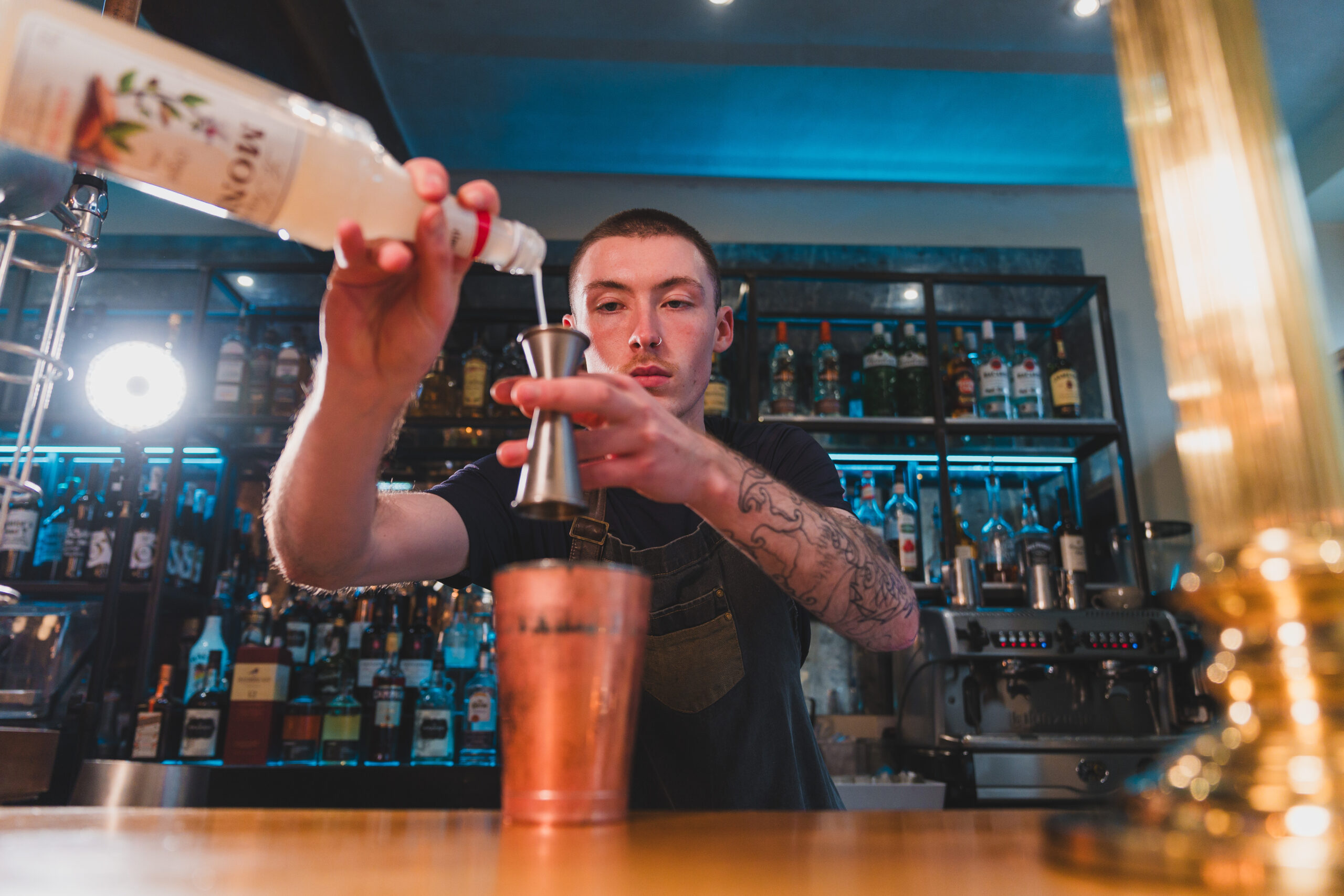 a man pouring into cocktail measurer at bar.